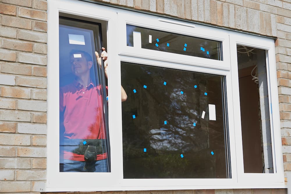 Home exterior showing a worker installing a replacement vinyl window, emphasizing window energy performance and thermal efficiency.